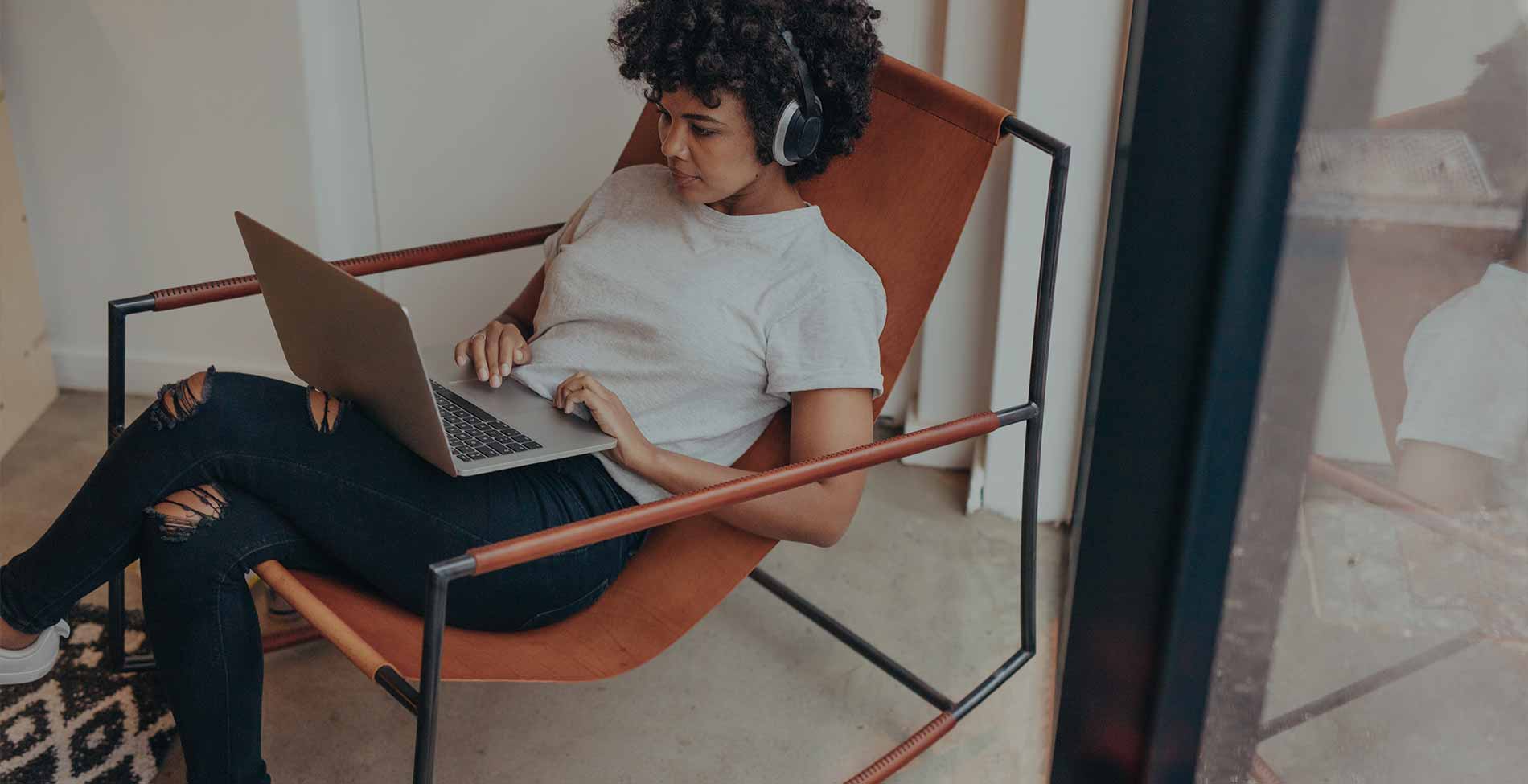 Person with curly hair using laptop while sitting on modern chair.